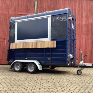 Mobiler Getränkewagen in Blau mit Holzblende und Menütafel, bereit für Events und Märkte.